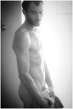 Black and white of a naked man standing in front of window holding towel with brilliant backlight